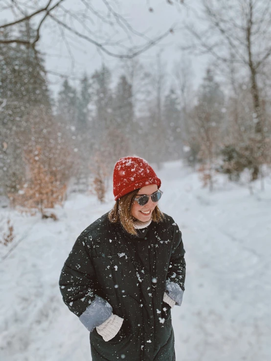  in sunglasses and red beanie smiles and laughs while walking through snow