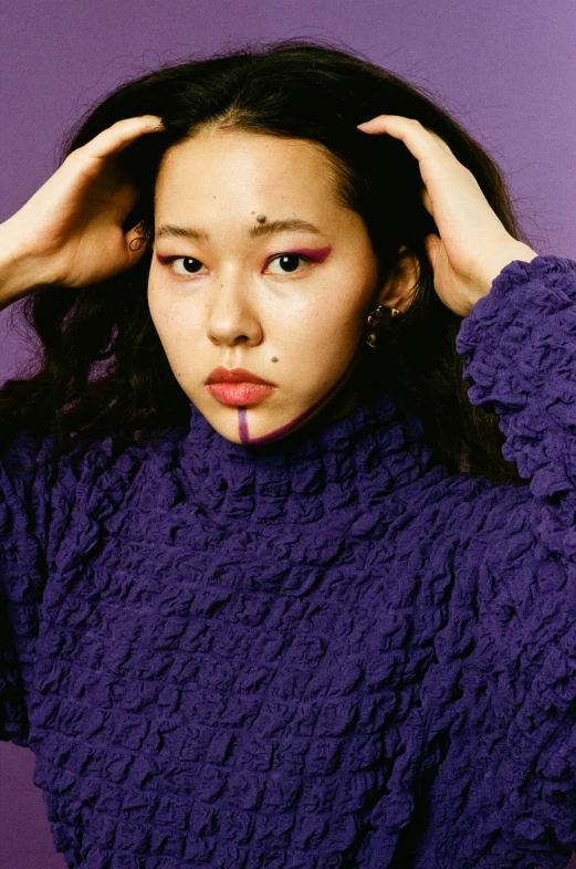 a woman standing against a purple background while wearing a knit shirt