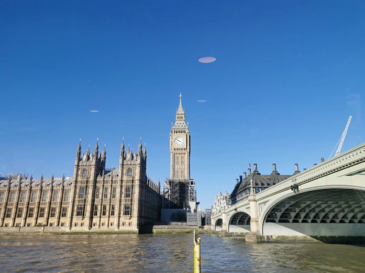 the large clock tower next to the water near a bridge