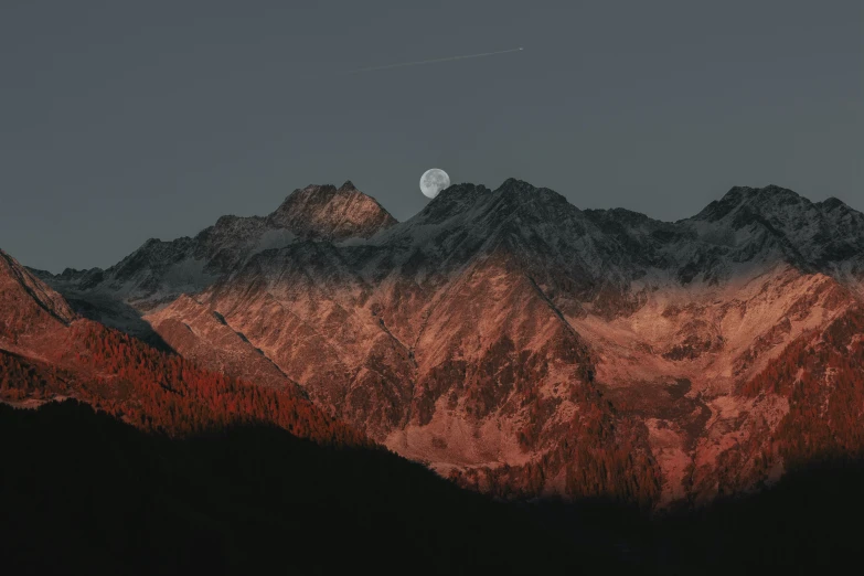 a red sun is setting on the mountains in front of the moon