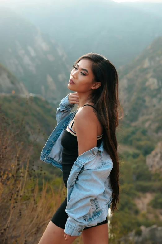 a young woman standing in the mountains wearing a jean jacket