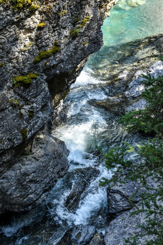 a person sitting on the side of a cliff near a stream