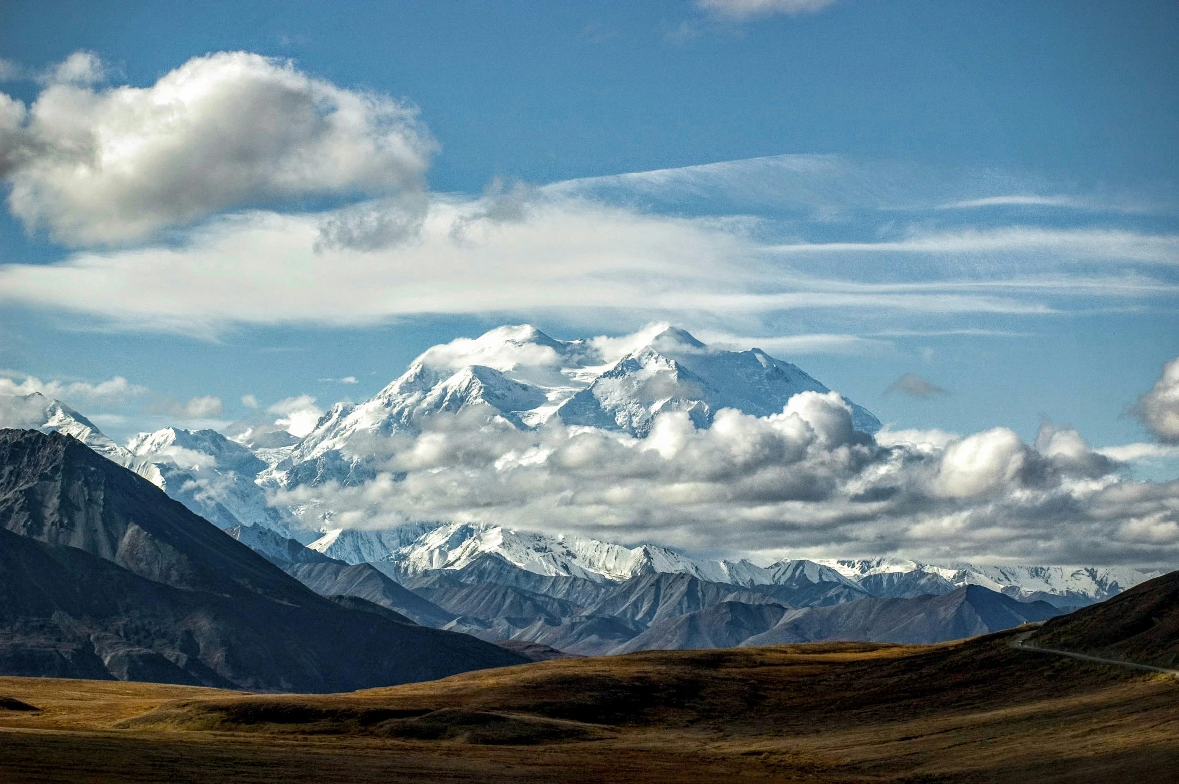 mountains with white snow and green grassy area under blue cloudy sky