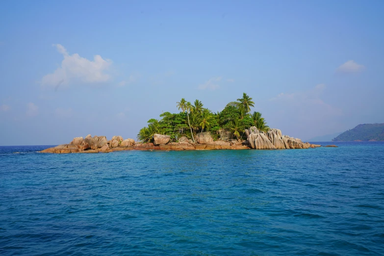 an island with trees on top in the middle of a body of water