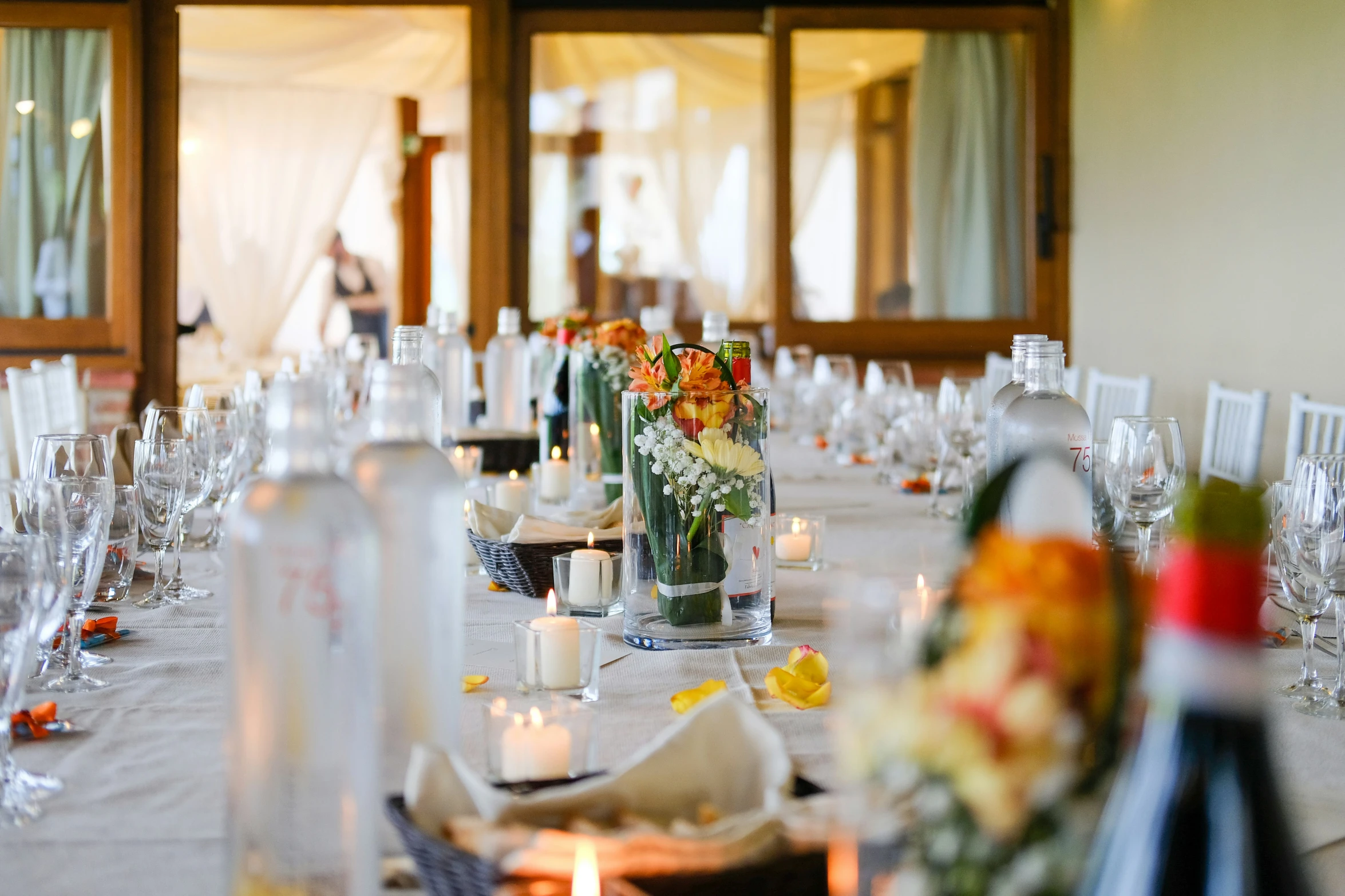 a dining table with clear wine glasses and vases of flowers