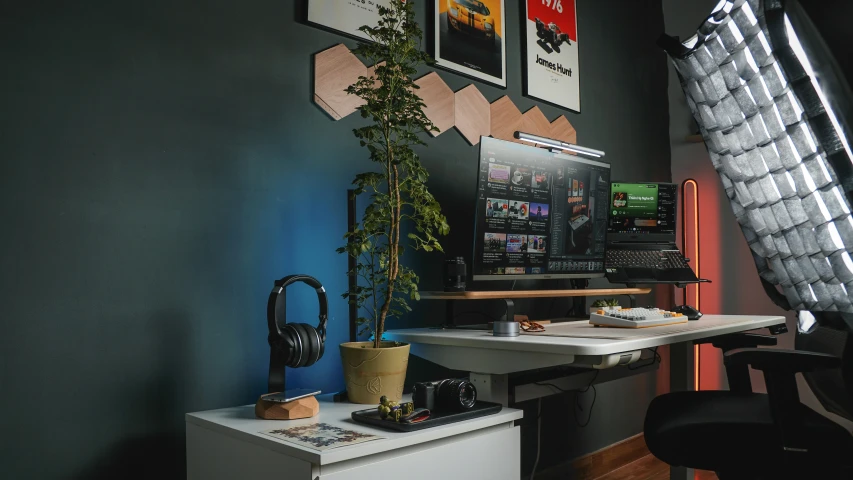 a desk with two computers, a plant and pictures on the wall