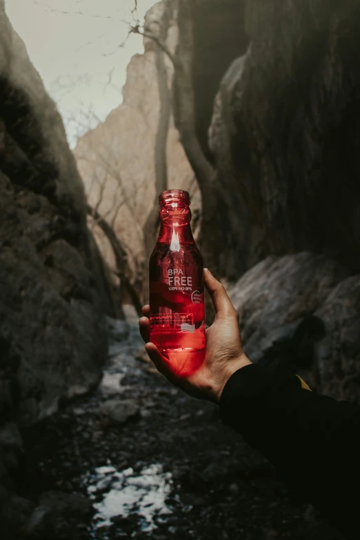 a man holding up a bottle of beer next to a cliff