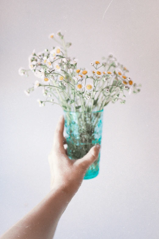a hand holding a vase with flowers in it