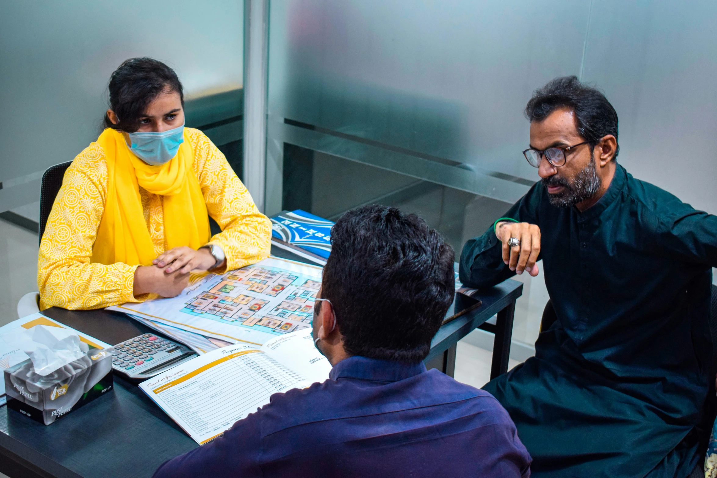 three people in the middle of an office are wearing masks