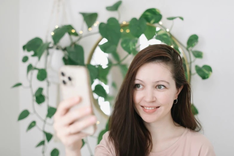 a beautiful young woman holding a smart phone in front of a mirror