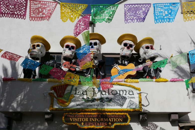 a group of sugar skulls with hats and tassels holding up a sign