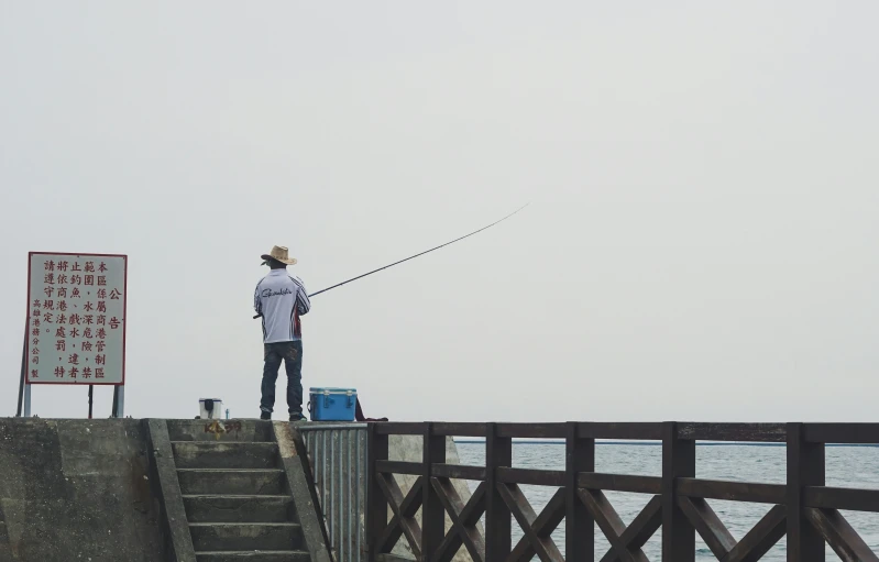 a person holding a fishing rod standing on a bridge