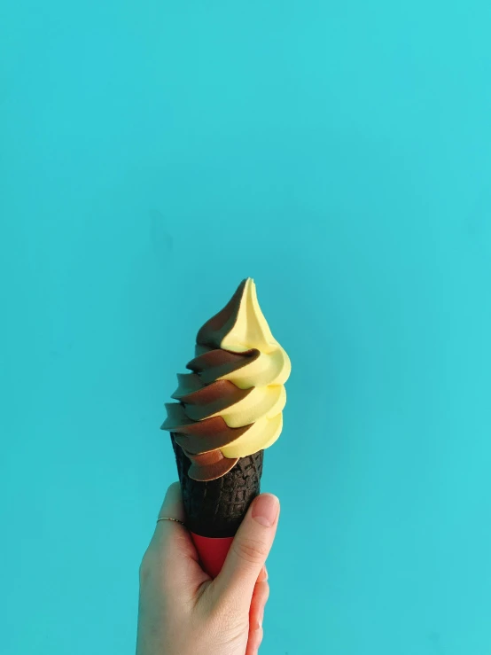 hand holding an unpeeled cupcake against a blue backdrop