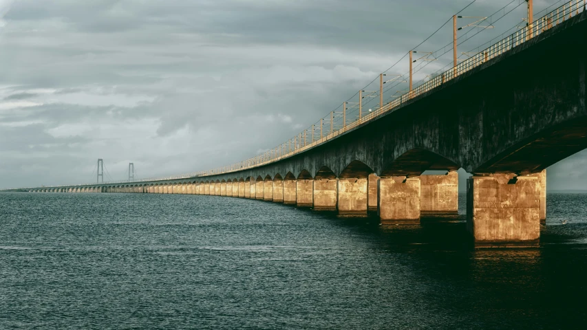 a large bridge spanning over the ocean under dark clouds