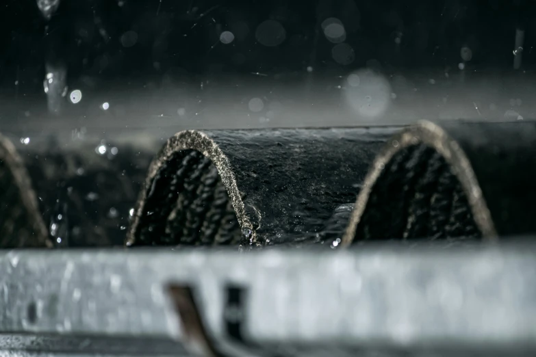 the bottom end of a metal barrel with rain droplets falling