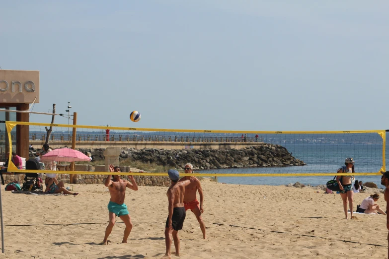 three people playing volleyball on a beach near the water