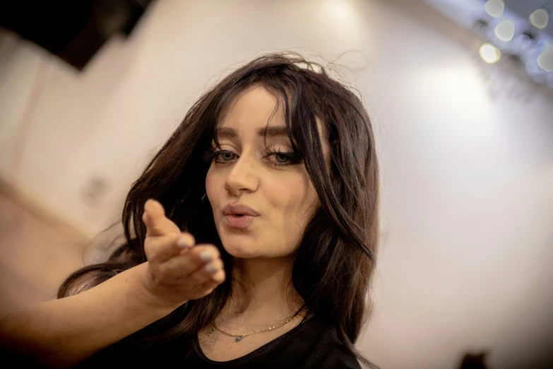 a woman with long hair wearing a black top with one hand out and one on her hip