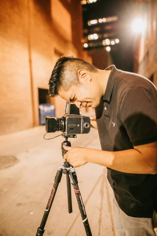 the man stands in front of the camera with his hand on a tripod