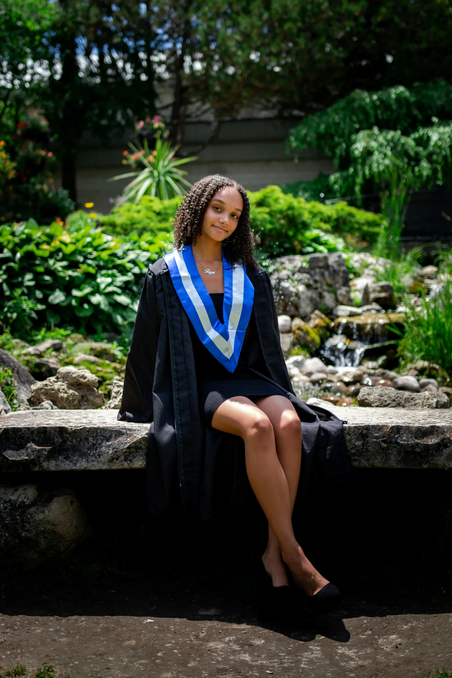 a woman sitting on a stone bench wearing a blue graduation robe