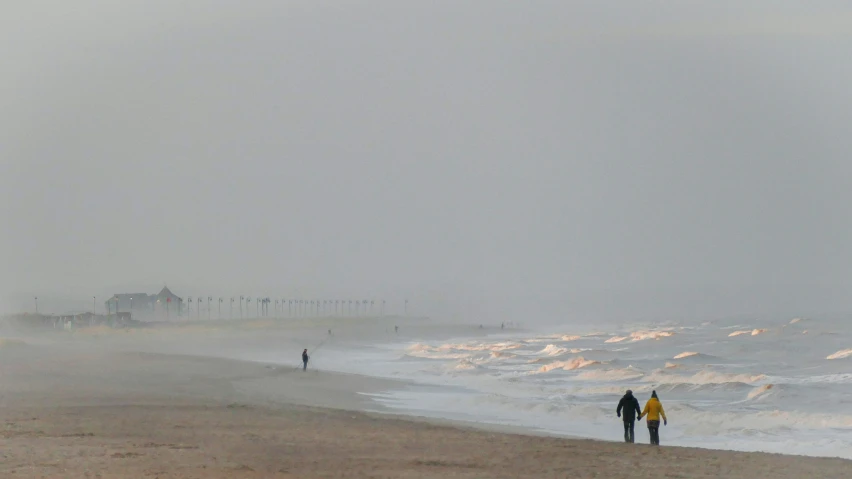 the people are walking along the beach in the foggy weather