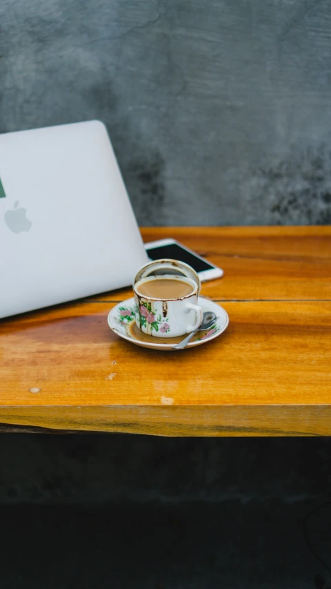 a cup and saucer next to a white apple laptop