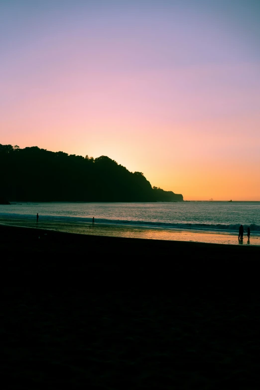 a silhouetted person stands on the beach at sunset