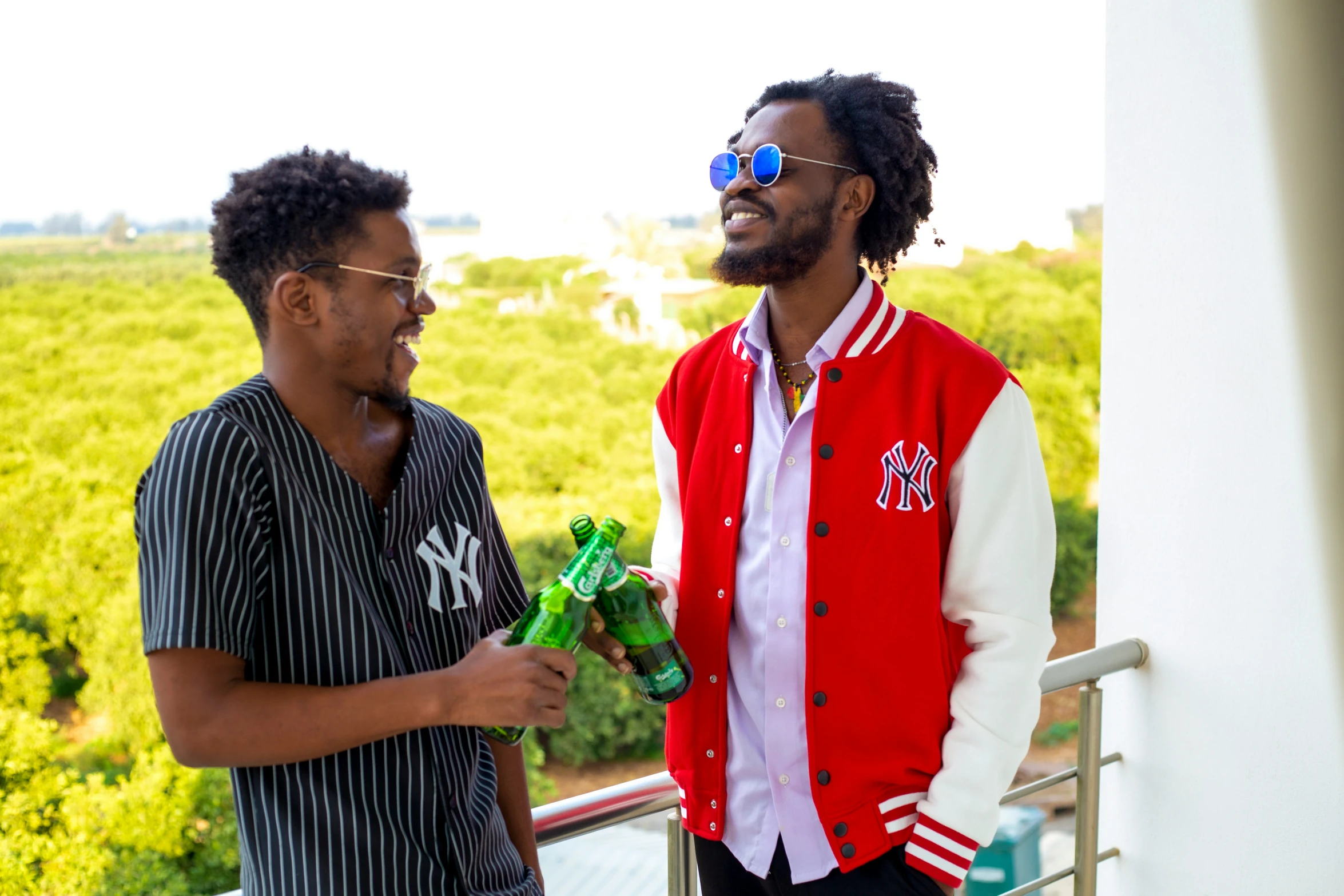 two men standing on a balcony with one holding a green bag and the other a red jacket