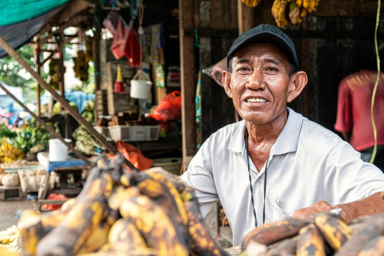 a man sitting at a fruit market surrounded by bananas