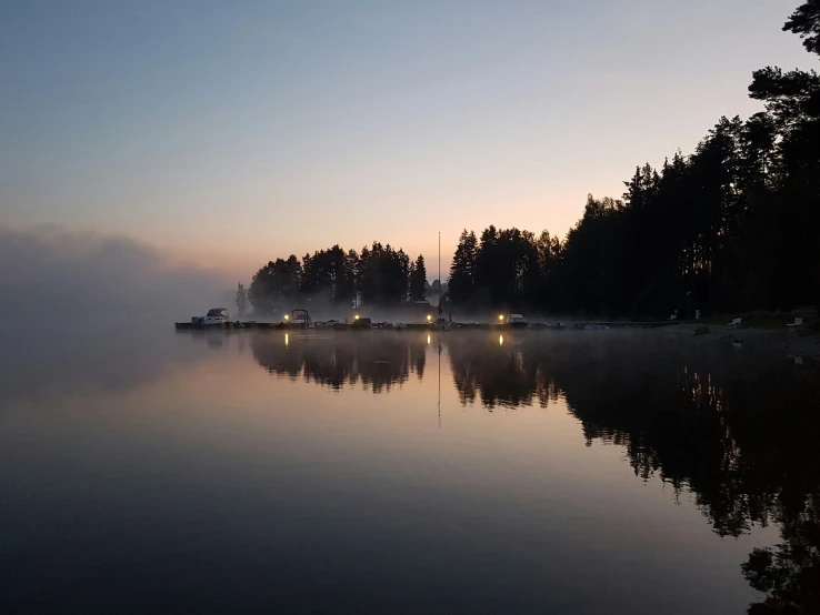 the sun is rising over some trees in the foggy lake