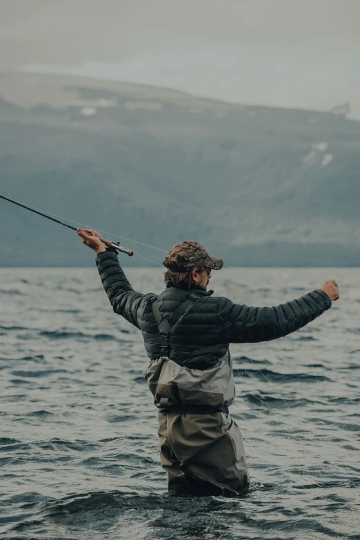 person in winter coat standing on the shore of lake, holding a fishing pole