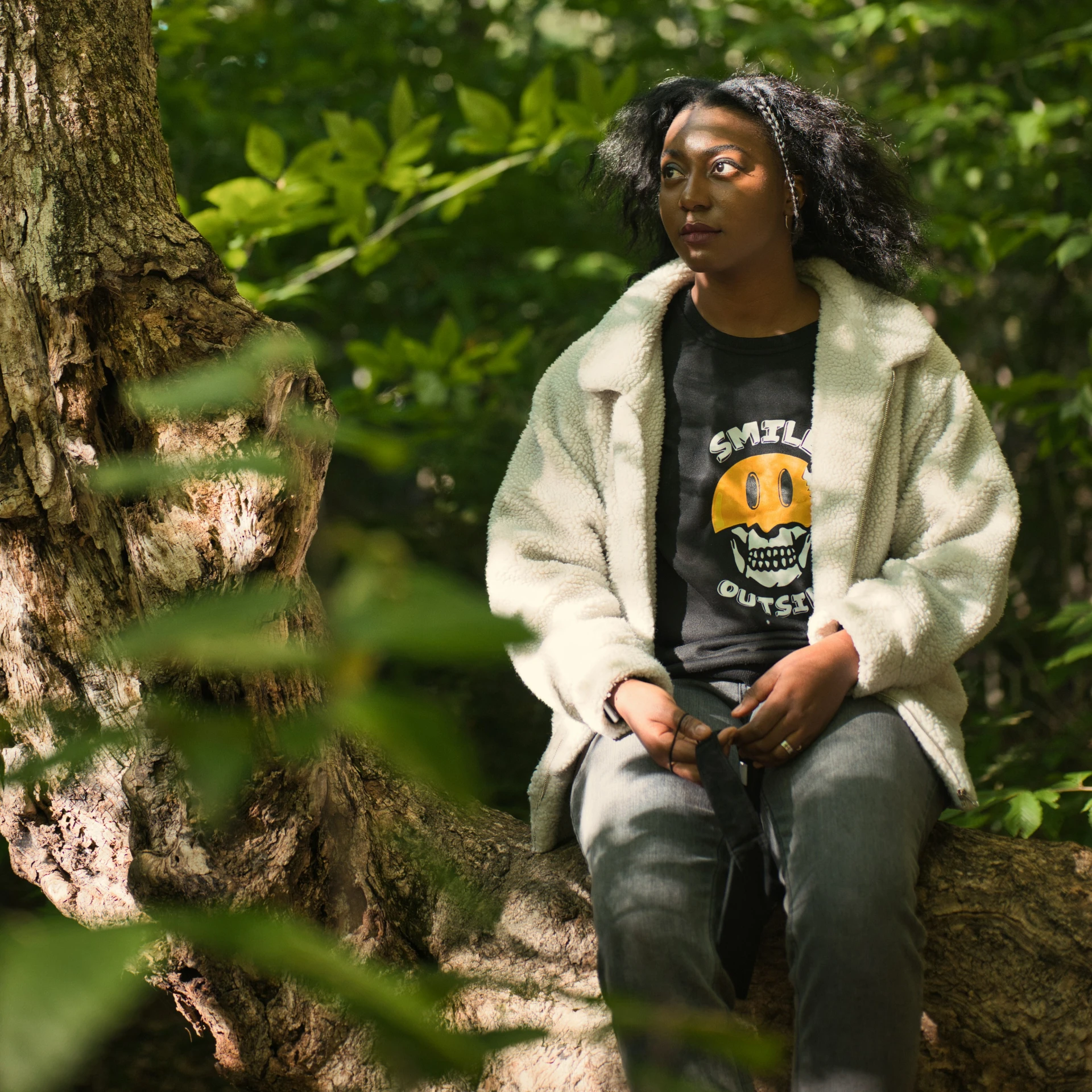 a girl in an oversized coat sits on a rock