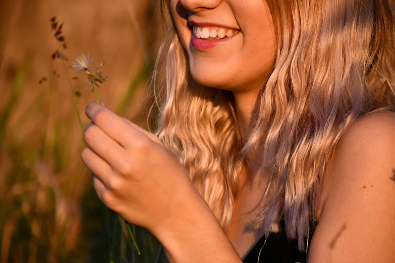a young blonde woman smiles while holding a flower
