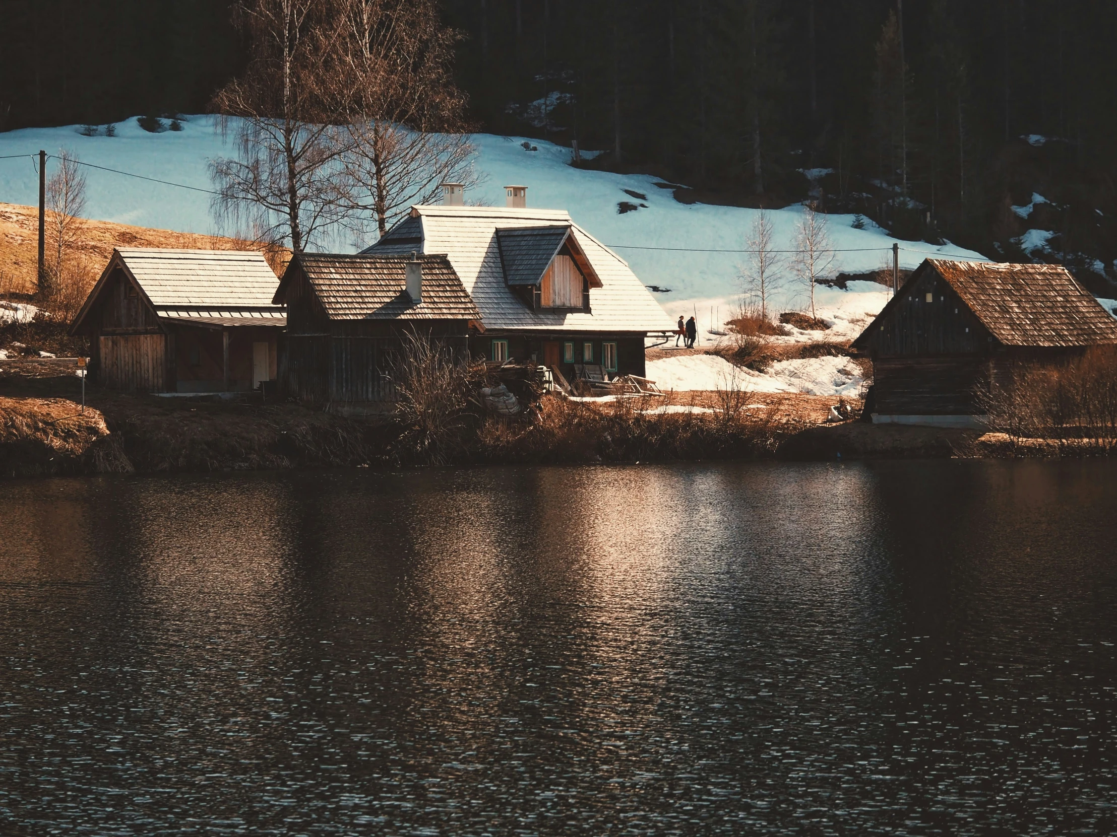 a house sits on the side of a lake in the mountains