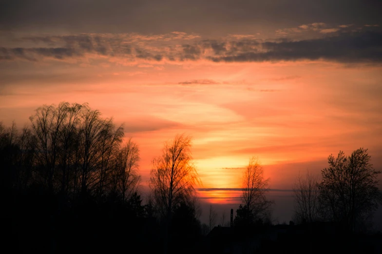 a sunset as seen through the clouds behind some trees