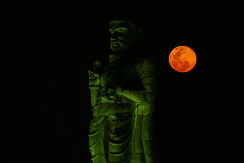 this is a statue and a large orange moon in the sky