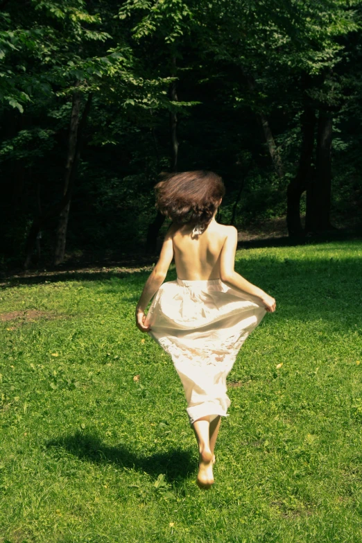 a woman is walking on the grass with her dress blowing in the wind