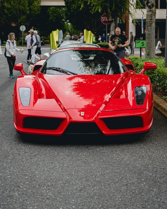 a red sports car parked on the street with people walking behind it