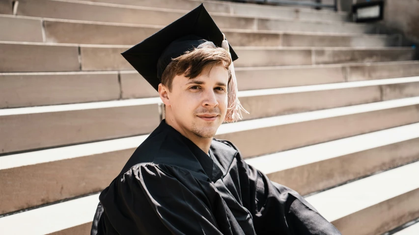 a man poses in his graduation gown on the bleachers
