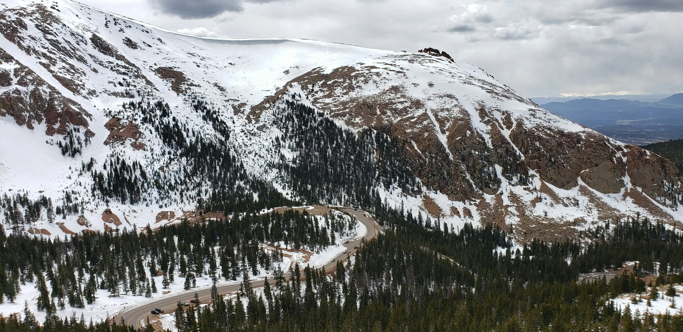 a very high snowy mountain with pine trees in front