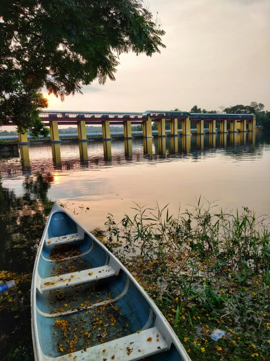 a blue rowboat in front of a lake and bridge