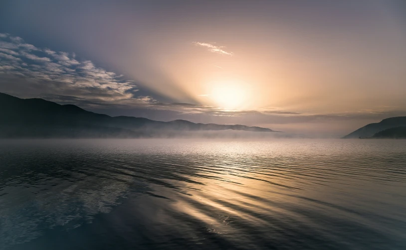 the sun rises over the mountains over a large lake