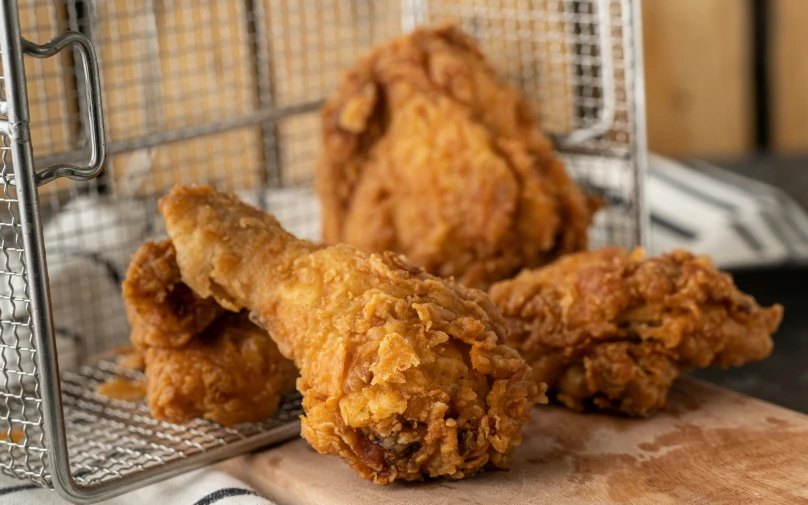 two chicken sticks on a board with the rest of a pair of fried chicken sticks in a metal basket