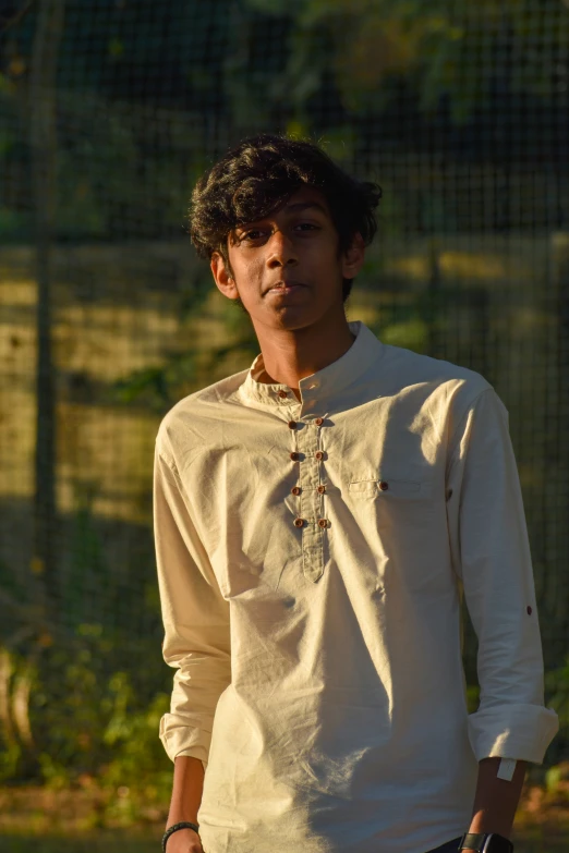 young man wearing white shirt in front of green and white fence