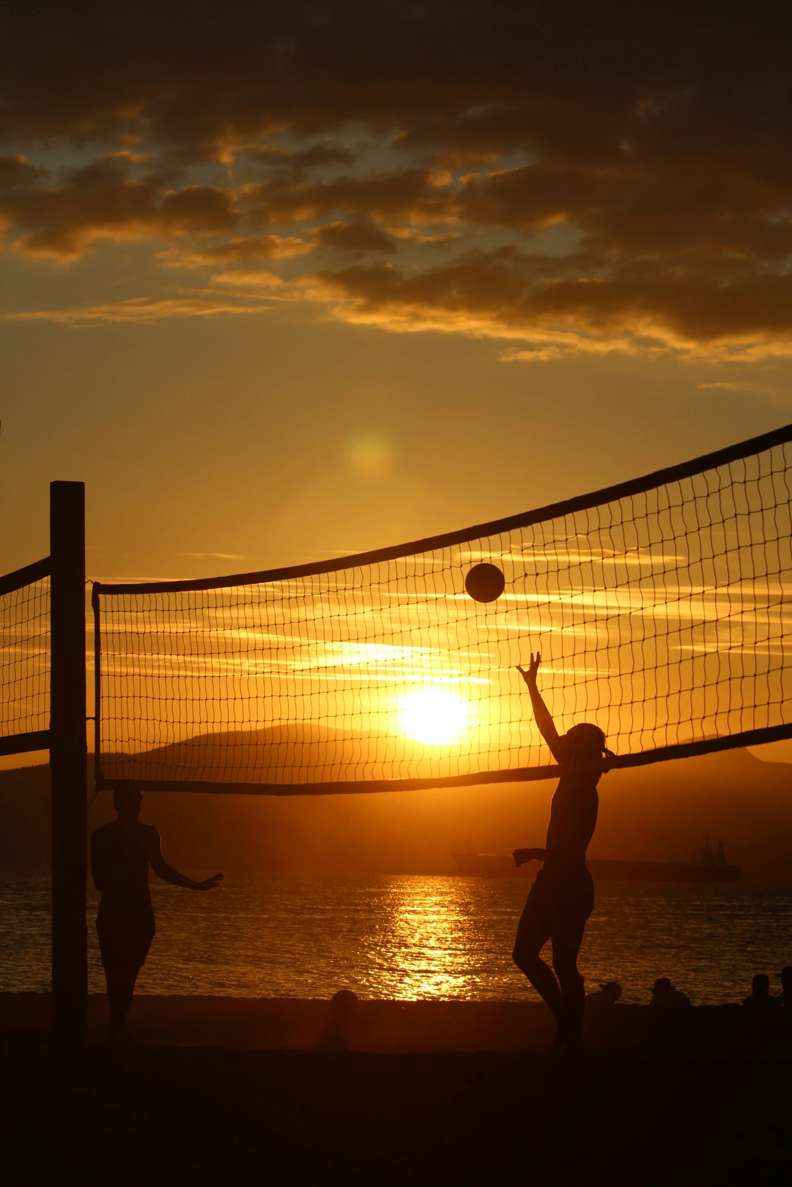 some people playing volleyball on a beach at sunset