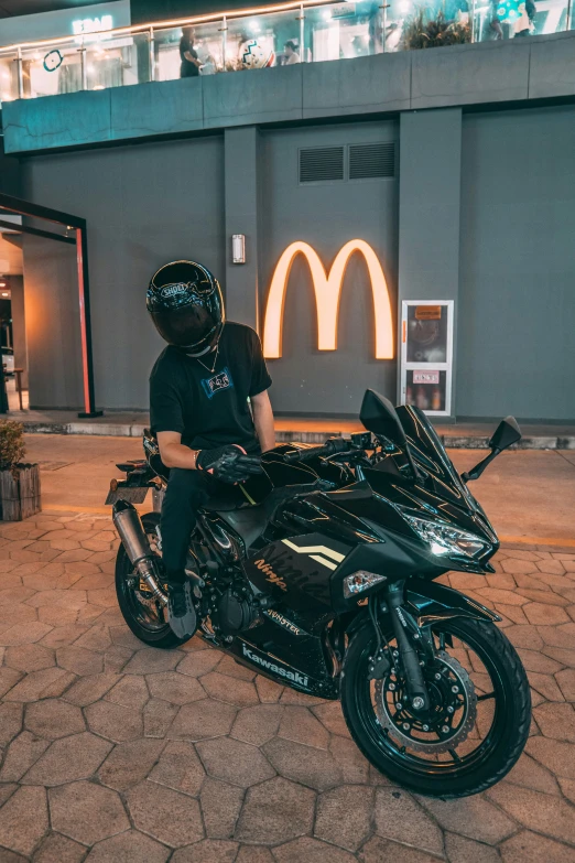 a man sitting on a parked motorcycle in front of a mcdonald's sign