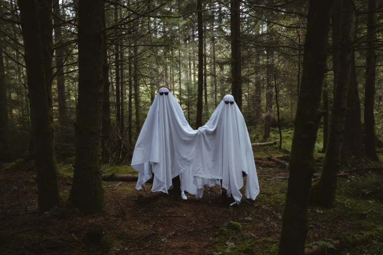 a couple dressed as ghost statues walking through the woods