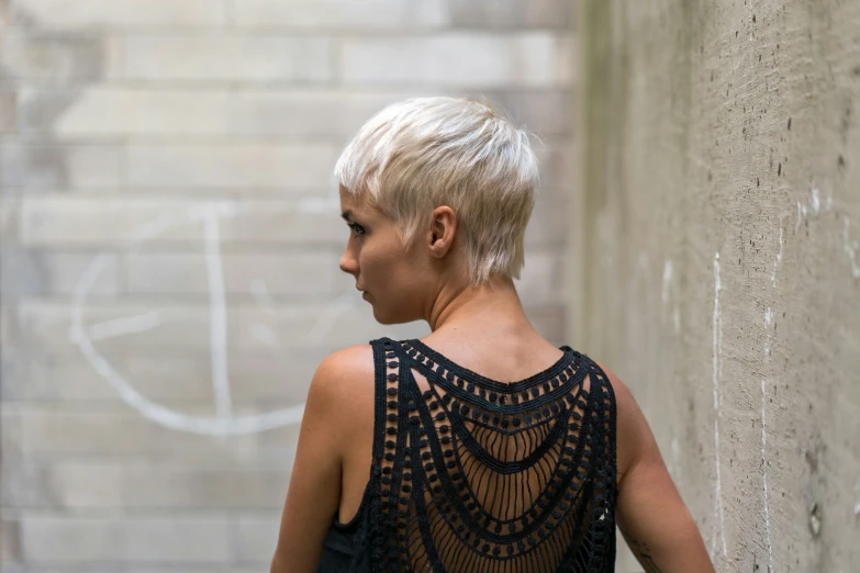 blonde woman with shaved back and dark shirt standing by wall