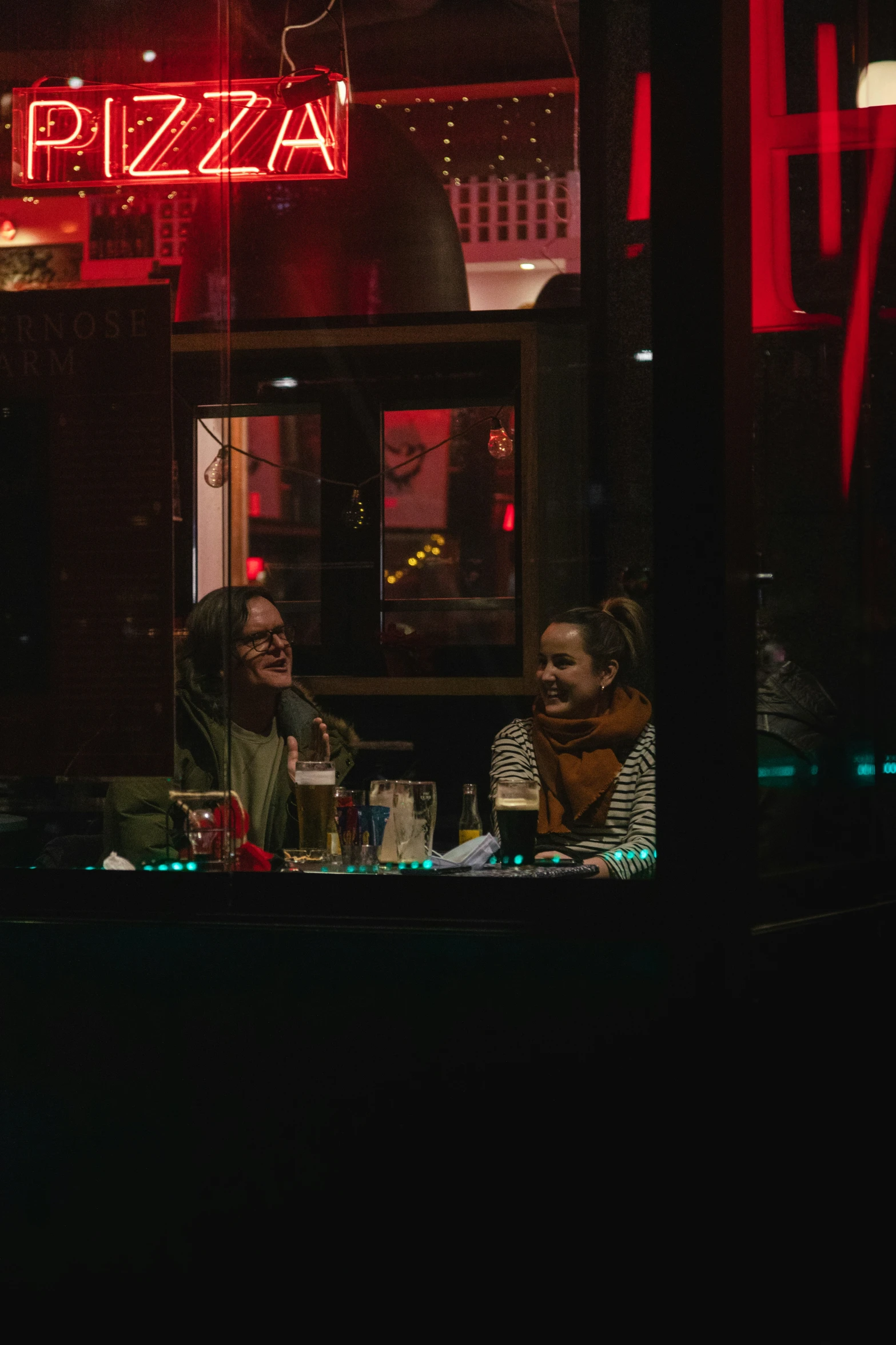 three people sitting at table outside of a pizza shop