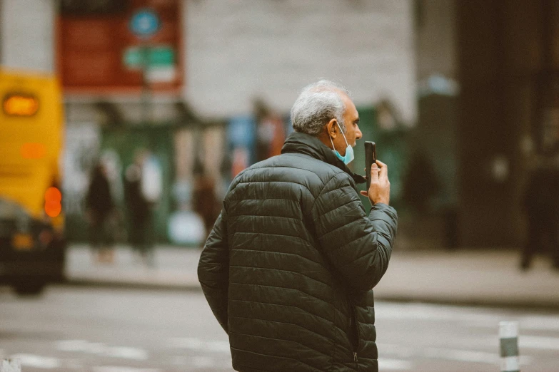 an older man standing on the side of a street talking on a cell phone