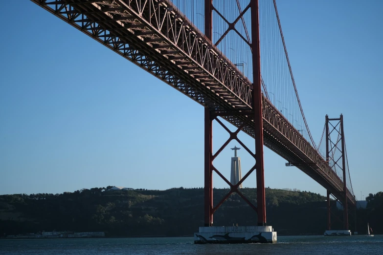 a boat floating under a suspension bridge on the water